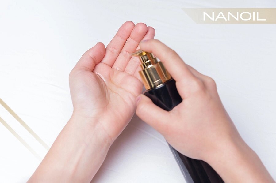 Detailný záber na ženské ruky držiace fľašu vlasového oleja Nanoil