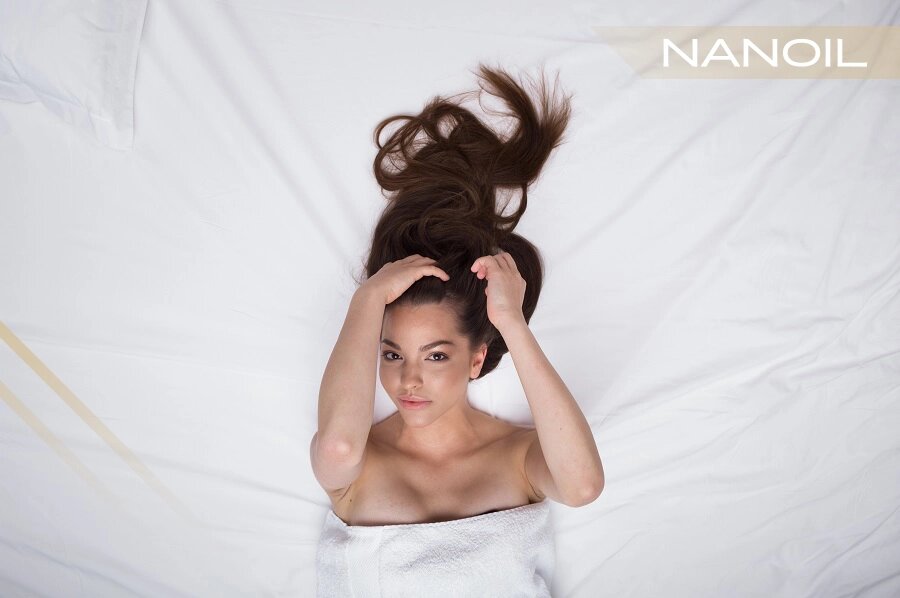 Žena v bielom uteráku leží na matraci a rukami si čistí vlasy